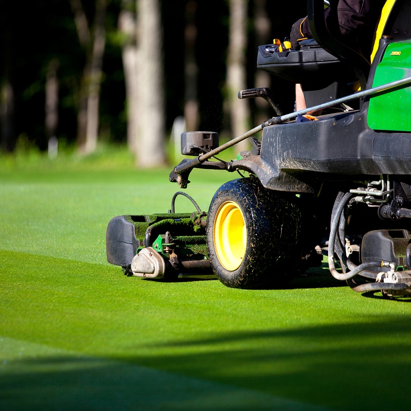 Tondeuse professionnelle John Deere entretient un gazon vert éclatant, laissant des stries nettes sur un green de golf.
